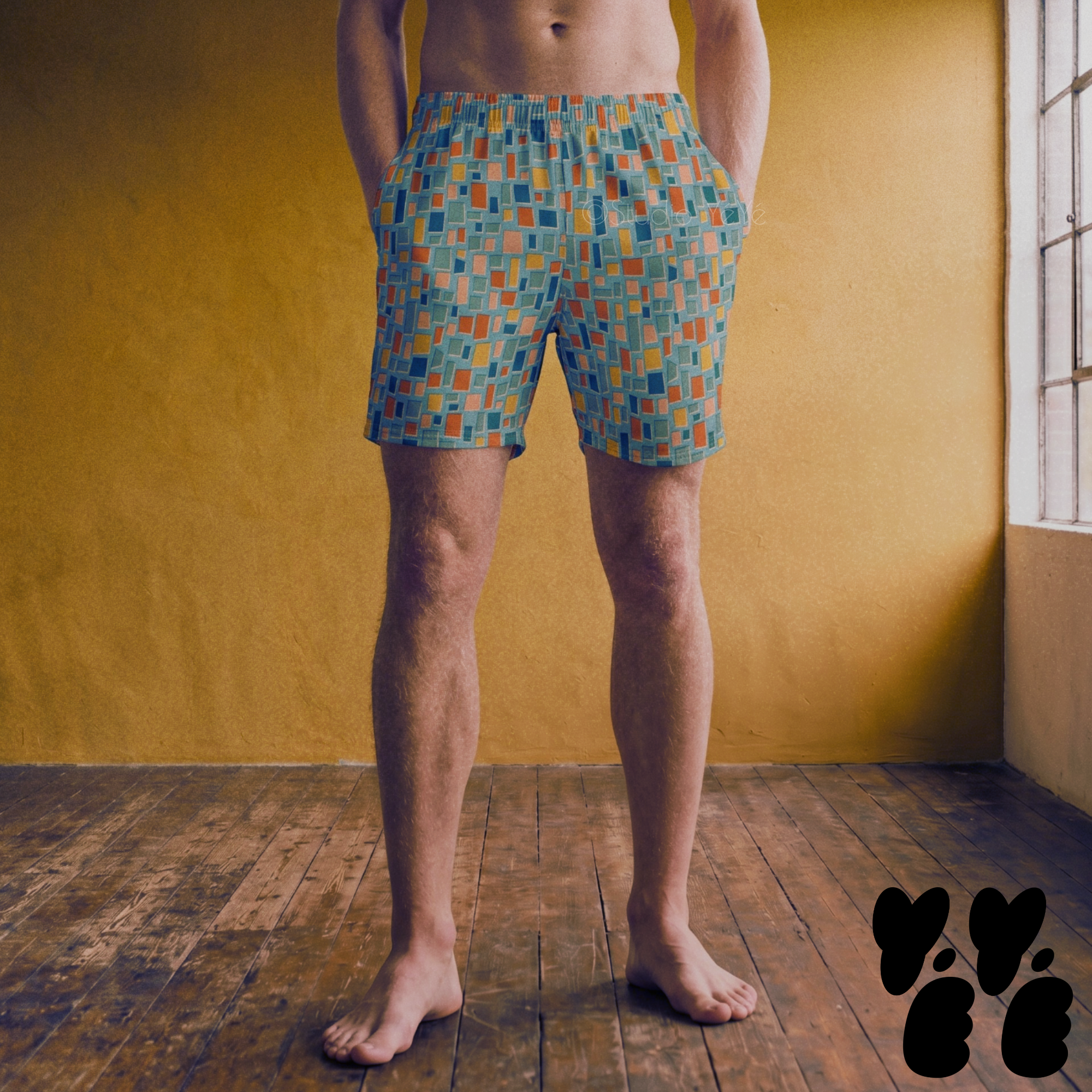 Model wearing mid-length swim trunks with a mid-century geometric mosaic tile pattern in teal blue, terracotta orange, mustard yellow, and muted pink.