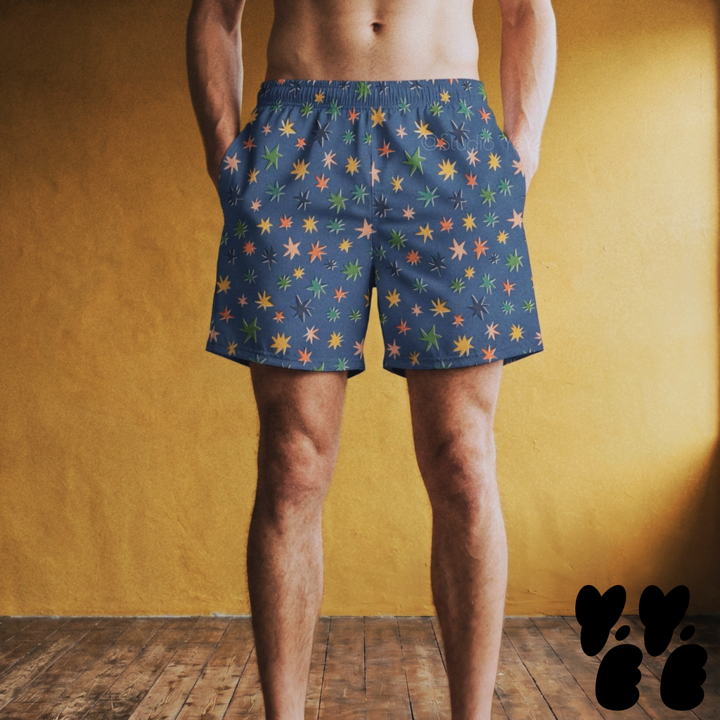 Model wearing mid-length swim trunks featuring a mid-century atomic starburst pattern with multi-colored retro stars on a deep blue background.