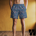 Model wearing mid-length swim trunks featuring a mid-century atomic starburst pattern with multi-colored retro stars on a deep blue background.