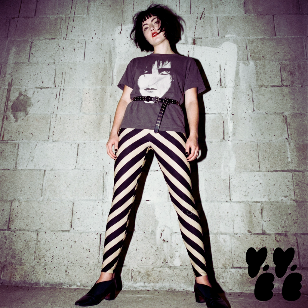 Model posing in black and cream diagonal stripe leggings with a post-punk aesthetic, styled with a leather jacket and Siouxsie Sioux graphic tee.