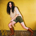 Model posing in green and brown stripe bike shorts, styled with an oversized beige t-shirt and vintage brown leather boots.