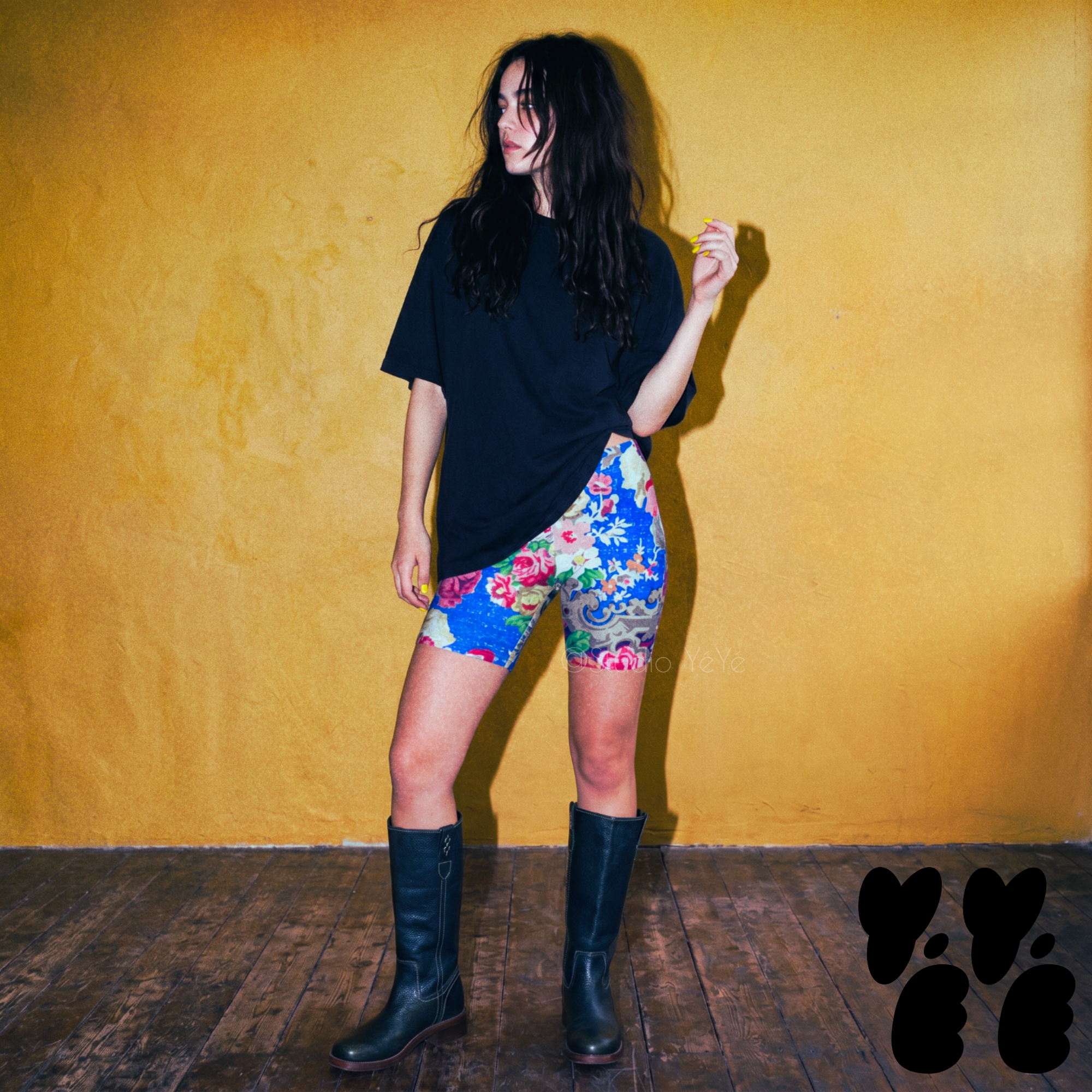 A female model wears 18th century rococo style floral printed bike shorts with oversized T-shirts and western boots 