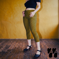 Model wearing dark mustard capri leggings with a navy blue polka dot pattern, styled with a black top and Mary Jane heels.