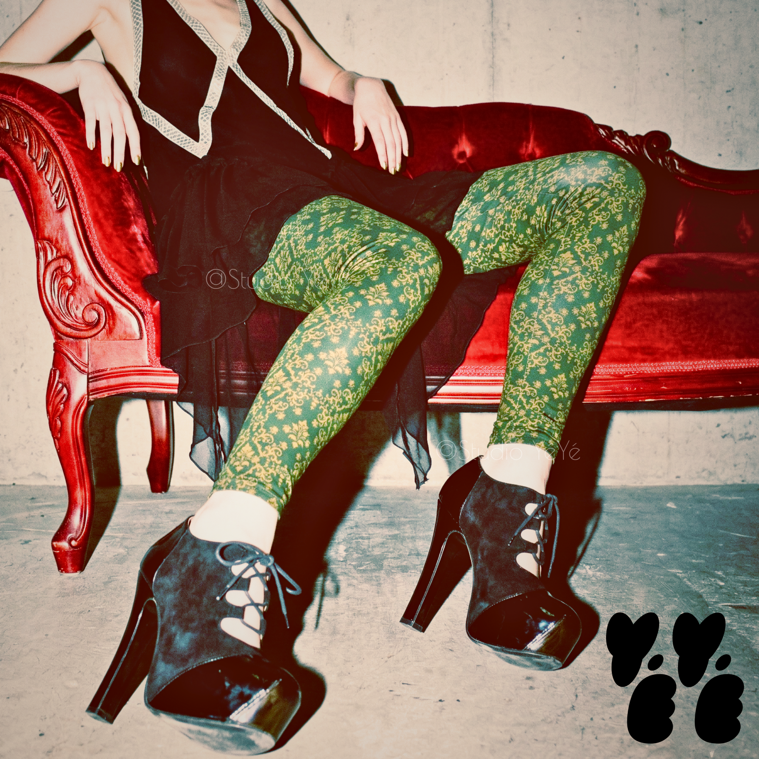 Dark green and gold damask print leggings by YéYé, styled with a black chiffon dress and black lace-up platform heels on a red velvet chaise longue