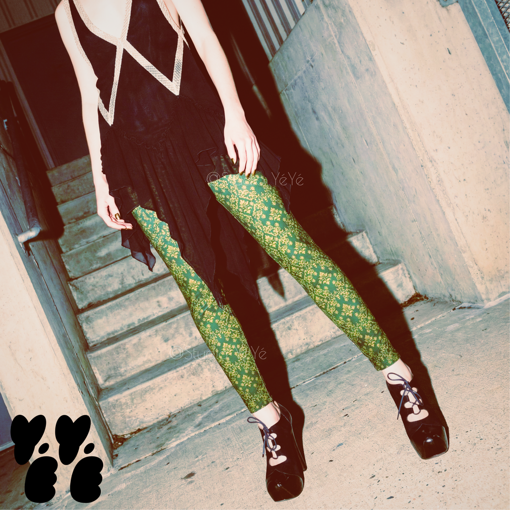 Green and gold vintage damask print leggings by YéYé, styled with a black chiffon dress and black lace-up platform heels on a red velvet chaise longue