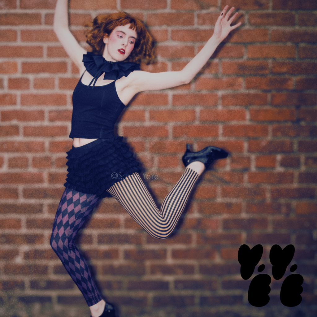 Model wearing eggplant purple and black harlequin diamond and fine pinstripe leggings with a black top and black shoes.