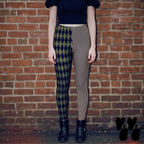 Model wearing olive green and black harlequin diamond and fine pinstripe leggings with a black top and black boots.