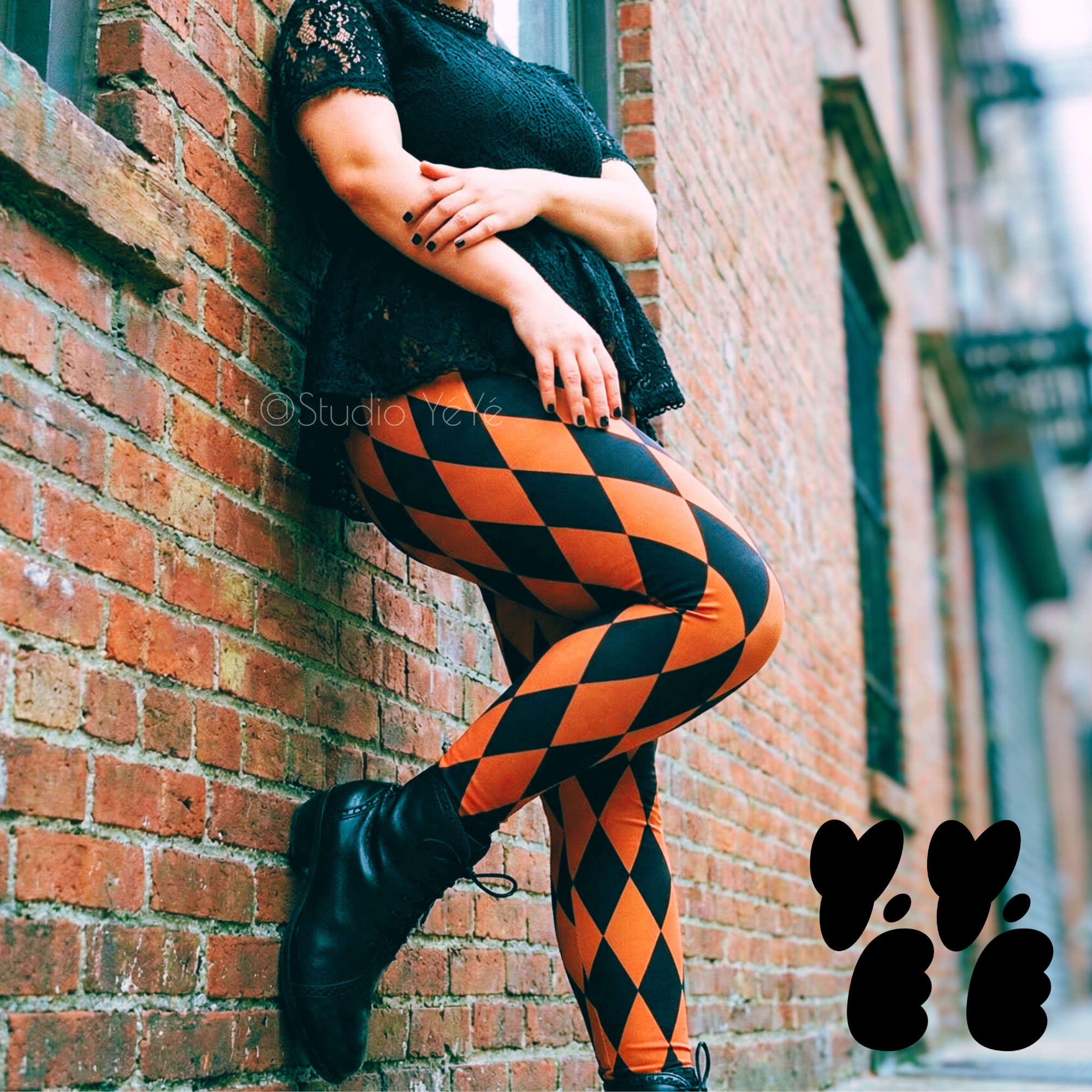 A plus size female model wears size 2XL harlequin diamond leggings in burnt orange-pumpkin and black, lace vintage top and victorian boots