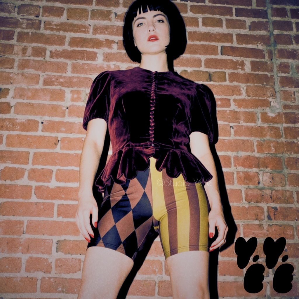 A female model wearing size S bike short in gold, black and burgundy jester style mismatched legs shorts, workout, layering, clowncore or any street fashion
