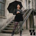 A plus size model wears black broomer, vintage lace top with jester leggings in olive and maroon, with victorian boots, goth punk vibe.