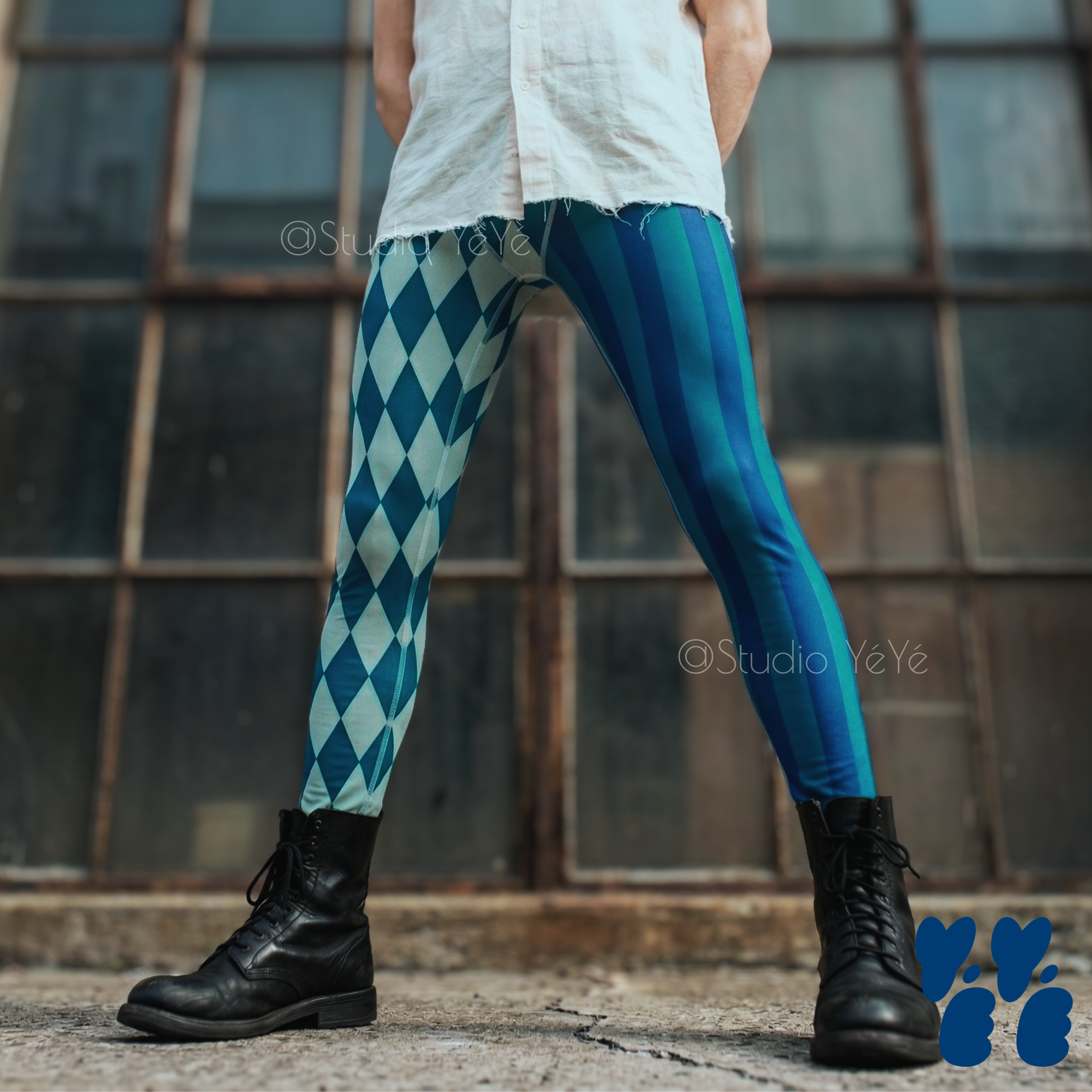 Blue and teal harlequin diamond and stripe mens leggings by YéYé, styled with a white linen shirt and black combat boots in front of industrial windows