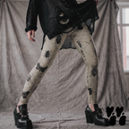 Model wearing beige vintage-inspired leggings covered with black beetles, moths, and insect illustrations, styled with black boots.