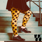 A plus sized female model wears 3XL large polka dot leggings in mustard yellow with black velvet dress and patent leather shoes