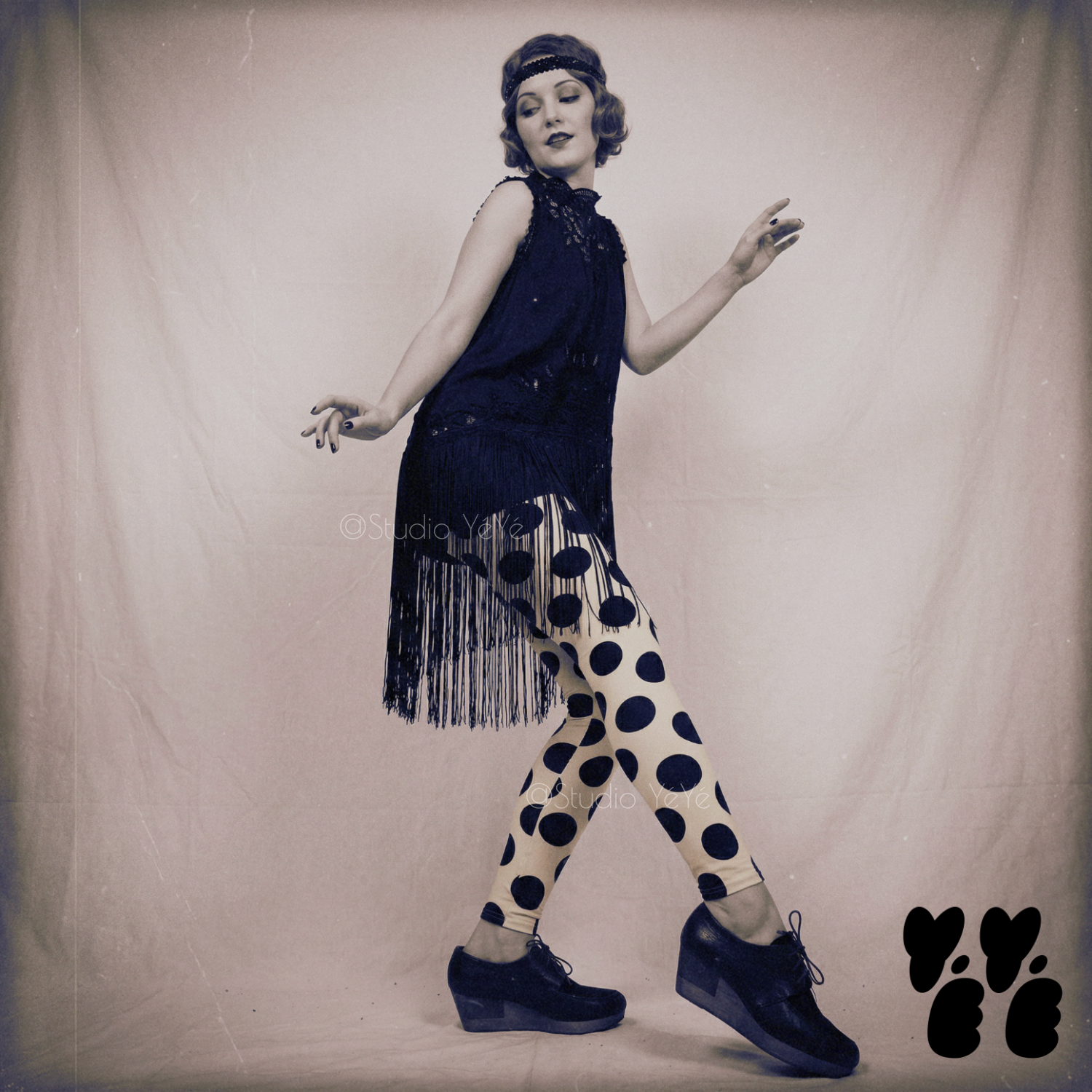 A flapper fashion girl wears 1930s vintage dress with large polka dot leggings with black platform shoes, posing like flapper dancer.
