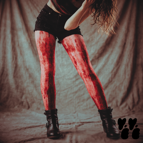 Model wearing red blood-splatter leggings styled with black shorts, a black top, and black ankle boots.