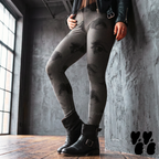 Model wearing black leggings covered with surreal eyes and tiny golden dots, styled with black boots and a leather jacket.