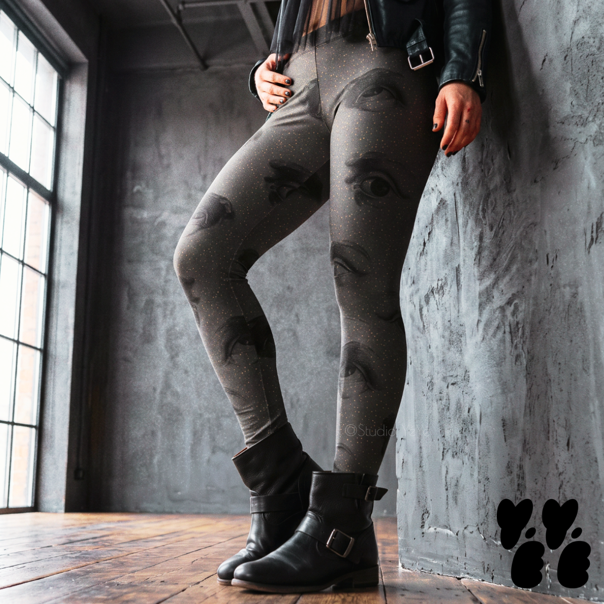 Model wearing black leggings covered with surreal eyes and tiny golden dots, styled with black boots and a leather jacket.
