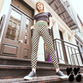A hipster model standing on steps in Soho NYC, in black and cream checkerboard leggings with a muted green and brown waistband and deep black side pockets, styled with black sneakers.
