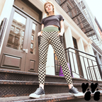 A hipster model standing on steps in Soho NYC, in black and cream checkerboard leggings with a muted green and brown waistband and deep black side pockets, styled with black sneakers.
