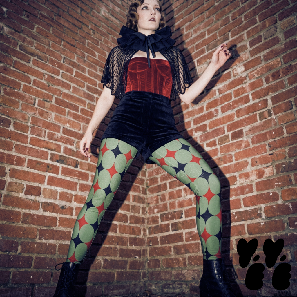 Model posing in olive green and black geometric starburst pattern fashion leggings with red diamond accents, styled in an alt mid-century circus aesthetic.