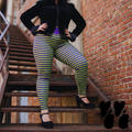 A plus size female model wears 2XL lime green and purple stripe leggings with gothic jacket