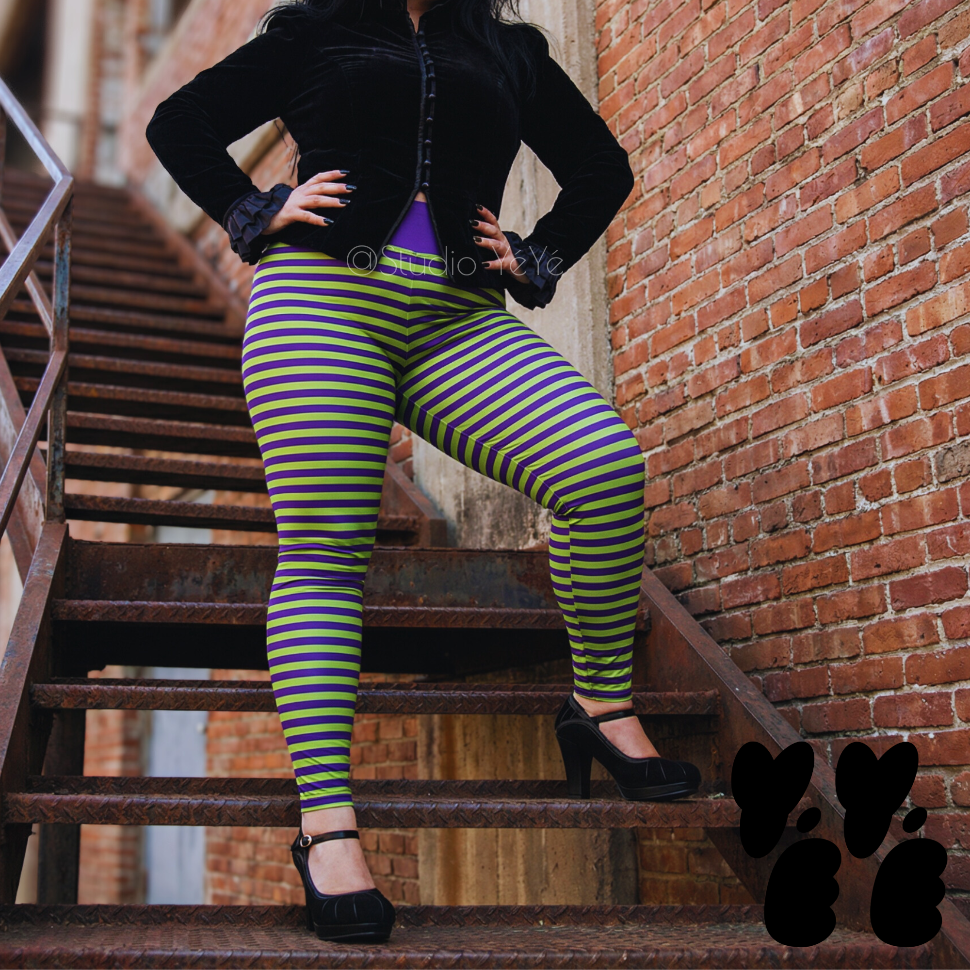 A plus size female model wears 2XL lime green and purple stripe leggings with gothic jacket