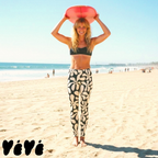 Vintage Hawaiian large floral print leggings in off-white and black by YéYé, styled with a black sports bra on the beach with a surfboard