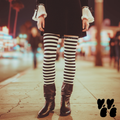 Black and white horizontal stripe leggings by YéYé, styled with a black mini skirt, white ruffle sleeve blouse and black slouch boots on a neon-lit city street at night