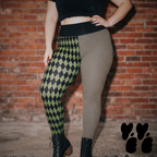 Model wearing olive green and black harlequin diamond and fine pinstripe leggings with a black top and black boots.