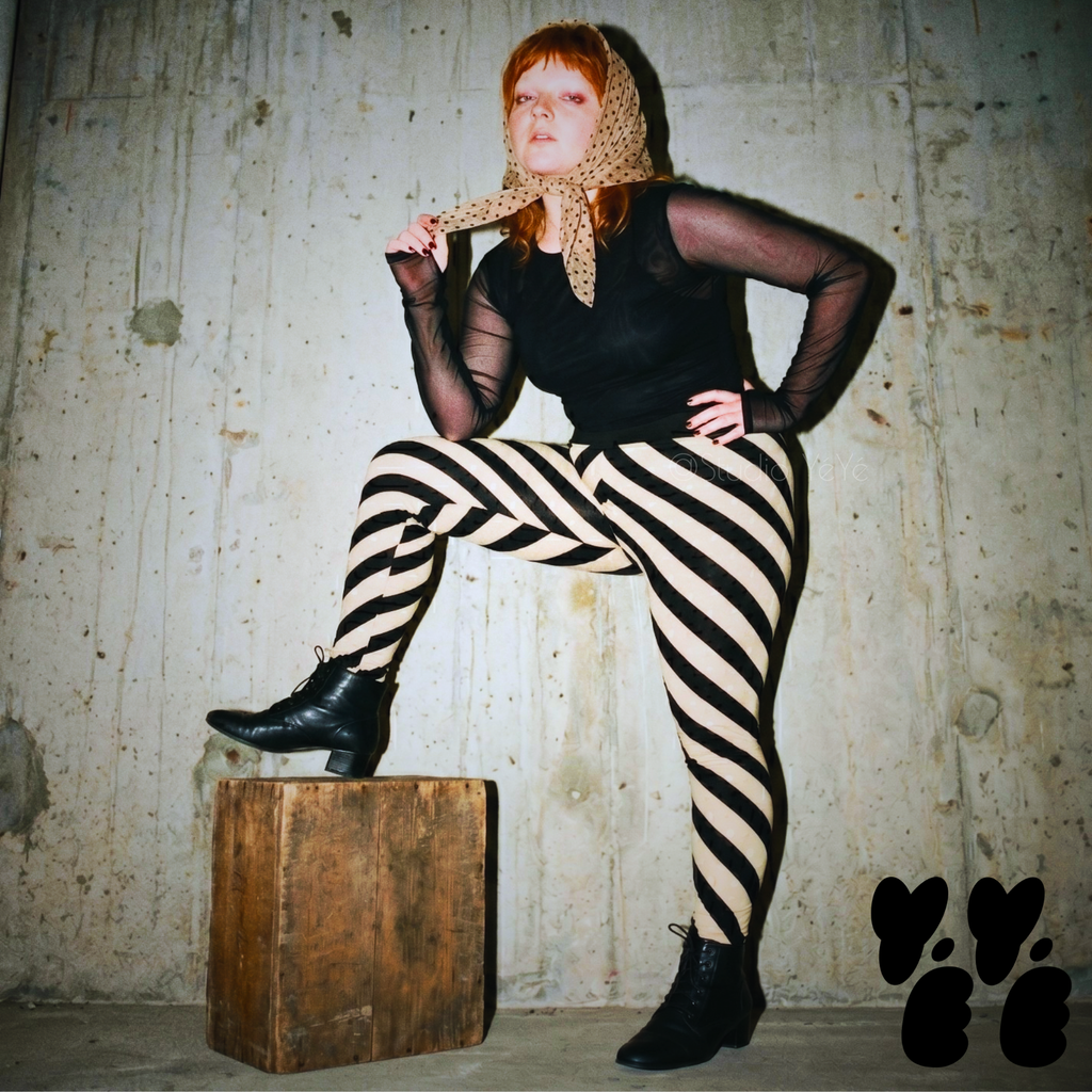 A hipster female plus size model wears diagonal bold stripe tights, 80's goth and punk vibe.