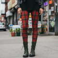 Red tartan plaid leggings by YéYé, styled with a black mini dress, black leather jacket and olive green lace-up combat boots on a city street