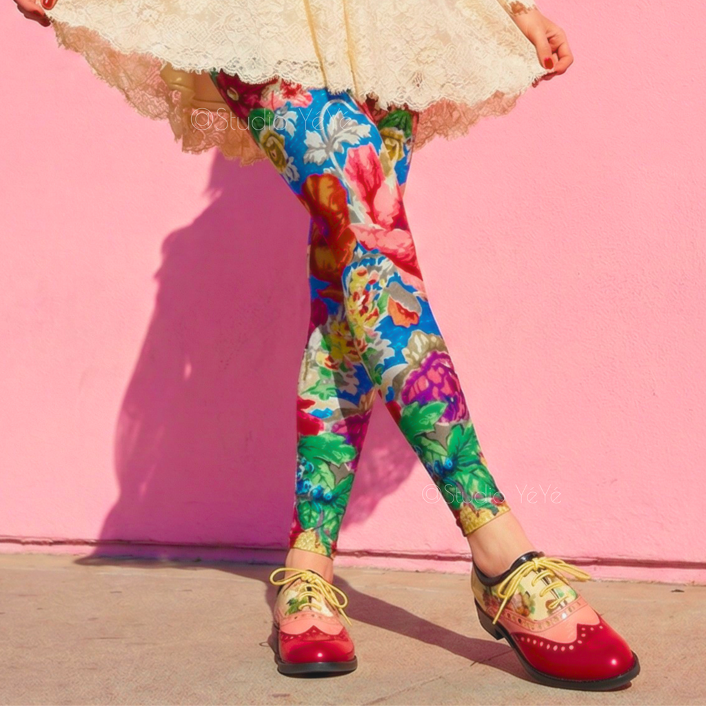 Vintage Rococo floral print leggings by YéYé in vibrant blue, red and green, styled with a cream lace mini dress, black ribbon choker and two-tone oxford shoes against a pink wall